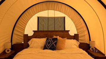 Una cama con cabecera de madera, dos mesitas de noche con lámparas y un reloj digital.