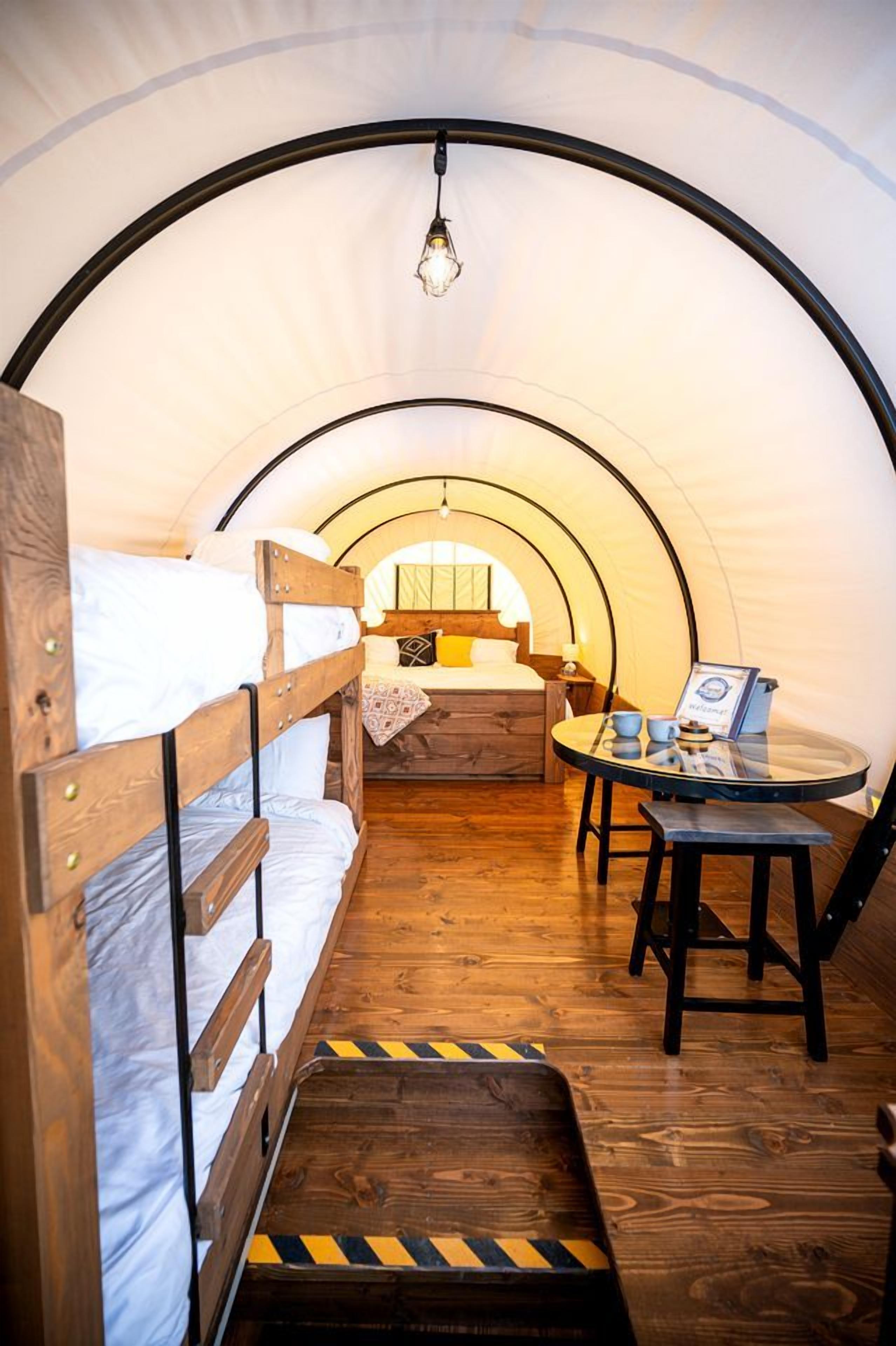 A tent with bunk beds, a small table with cups, and a hanging light fixture.