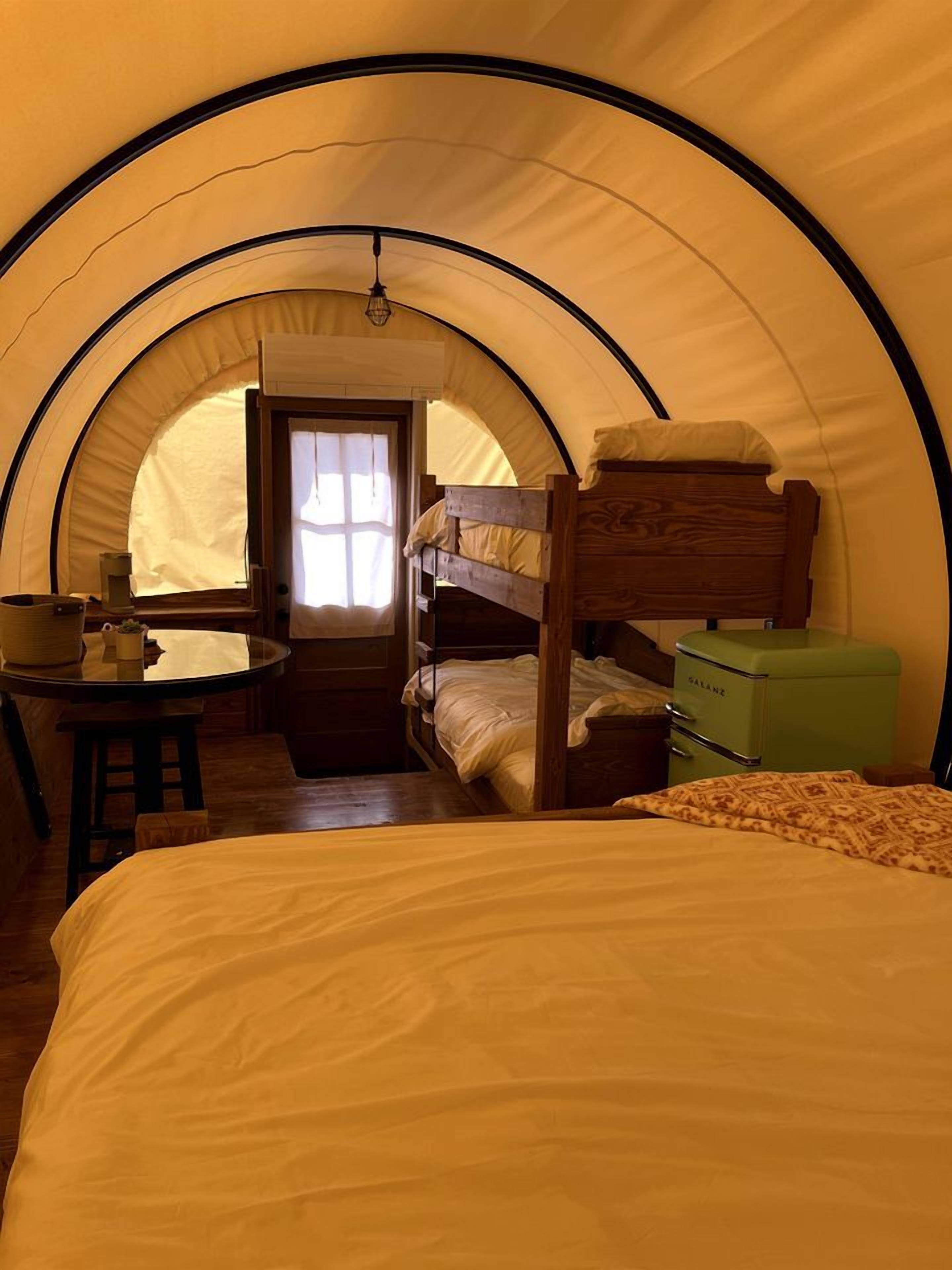 Una tenda con un letto a castello, un tavolino con una lampada e una valigia verde.