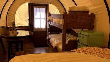 Una tenda con un letto a castello, un tavolino con una lampada e una valigia verde.