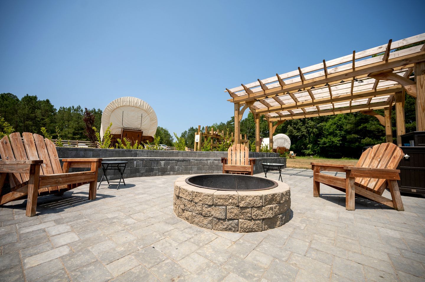 An outdoor patio with Adirondack chairs, a stone fire pit, and a wooden pergola.