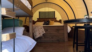 Een tent met stapelbedden, een tafel en een hanglamp.