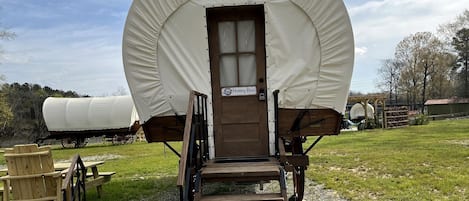 En overdækket vogn med en trädør mærket 'Honey Bee', en trærampe og et picnicbord i en græsmark.