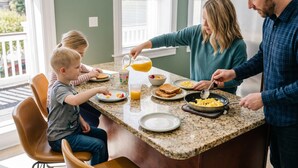 A family breakfast at a kitchen counter with a granite countertop, a window with blinds, and a view of greenery outside. - Near Forest Park & Central West End - Sleeps 6 (St. Louis)