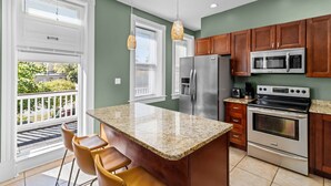 A kitchen with a central island, stainless steel appliances, wooden cabinets, and a balcony with outdoor seating. - Near Forest Park & Central West End - Sleeps 6 (St. Louis)