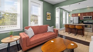 A modern living room with a sofa, coffee table, and a kitchen area with a bar and appliances. - Near Forest Park & Central West End - Sleeps 6 (St. Louis)