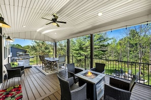 Eine überdachte Terrasse im Freien mit Grill, Esstisch, Stühlen und einem Feuerkorb.