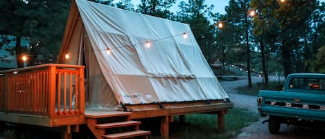 Una carpa con una terraza de madera y escalones, rodeada de árboles y un camino de grava.