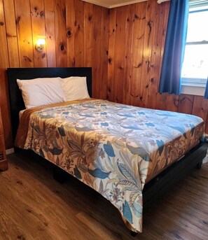 Ein Zimmer mit Holzwänden, einem Bett, einem Nachttisch und einer Wandleuchte.