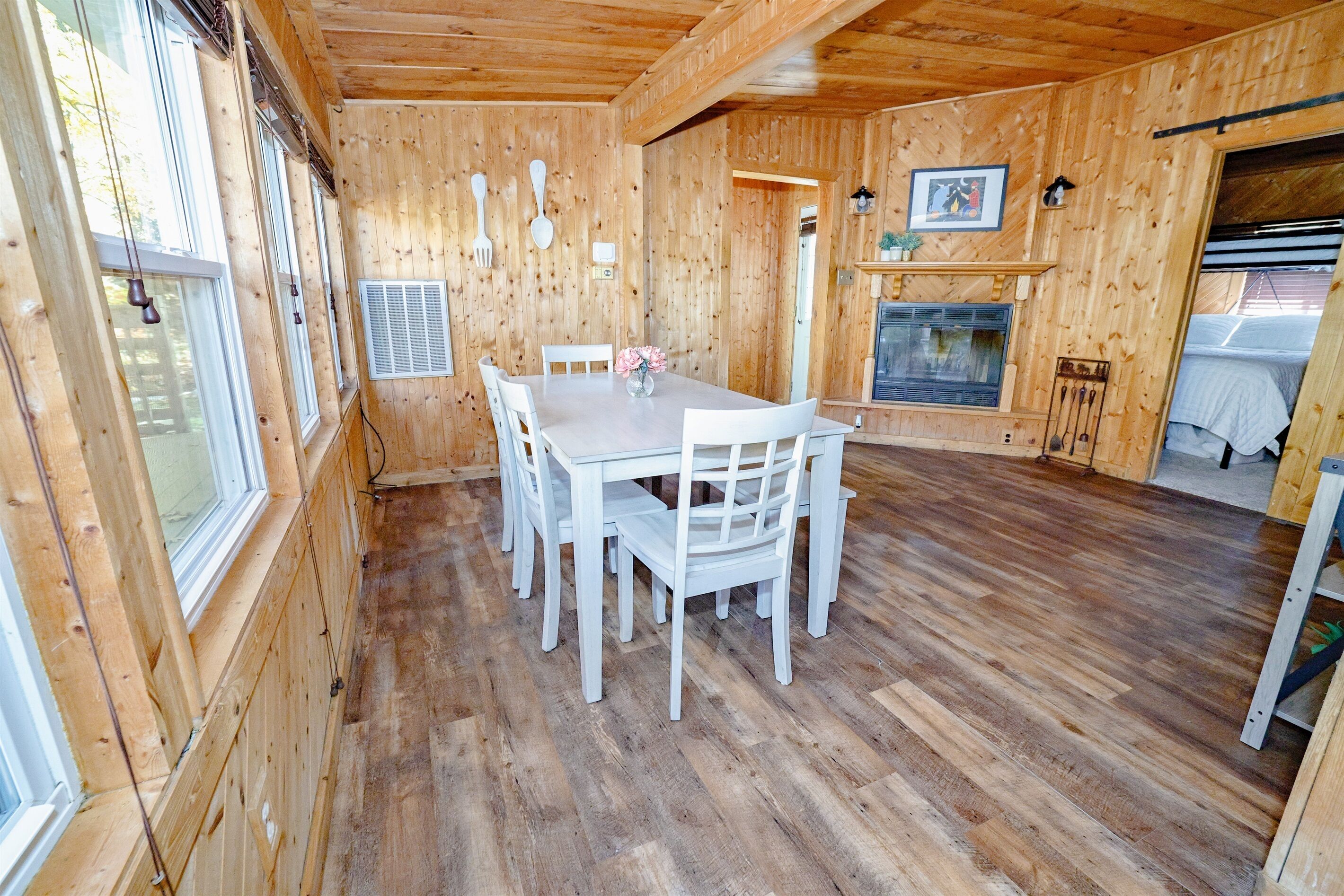 A wooden interior with a dining table, chairs, a fireplace, and a window.