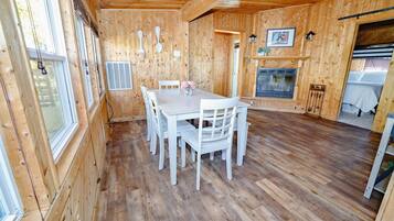 A wooden interior with a dining table, chairs, a fireplace, and a window.