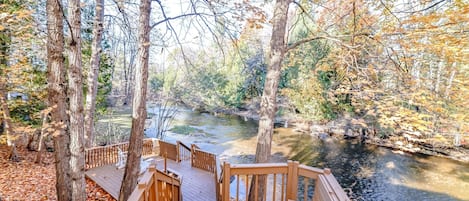 A wooden deck overlooking a river with trees and autumn leaves.