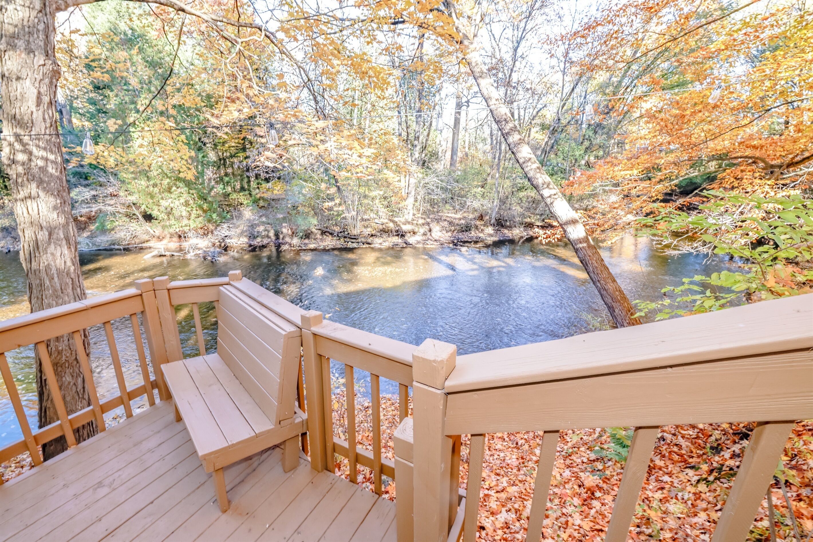 A wooden deck with a bench overlooking a river surrounded by autumn foliage.