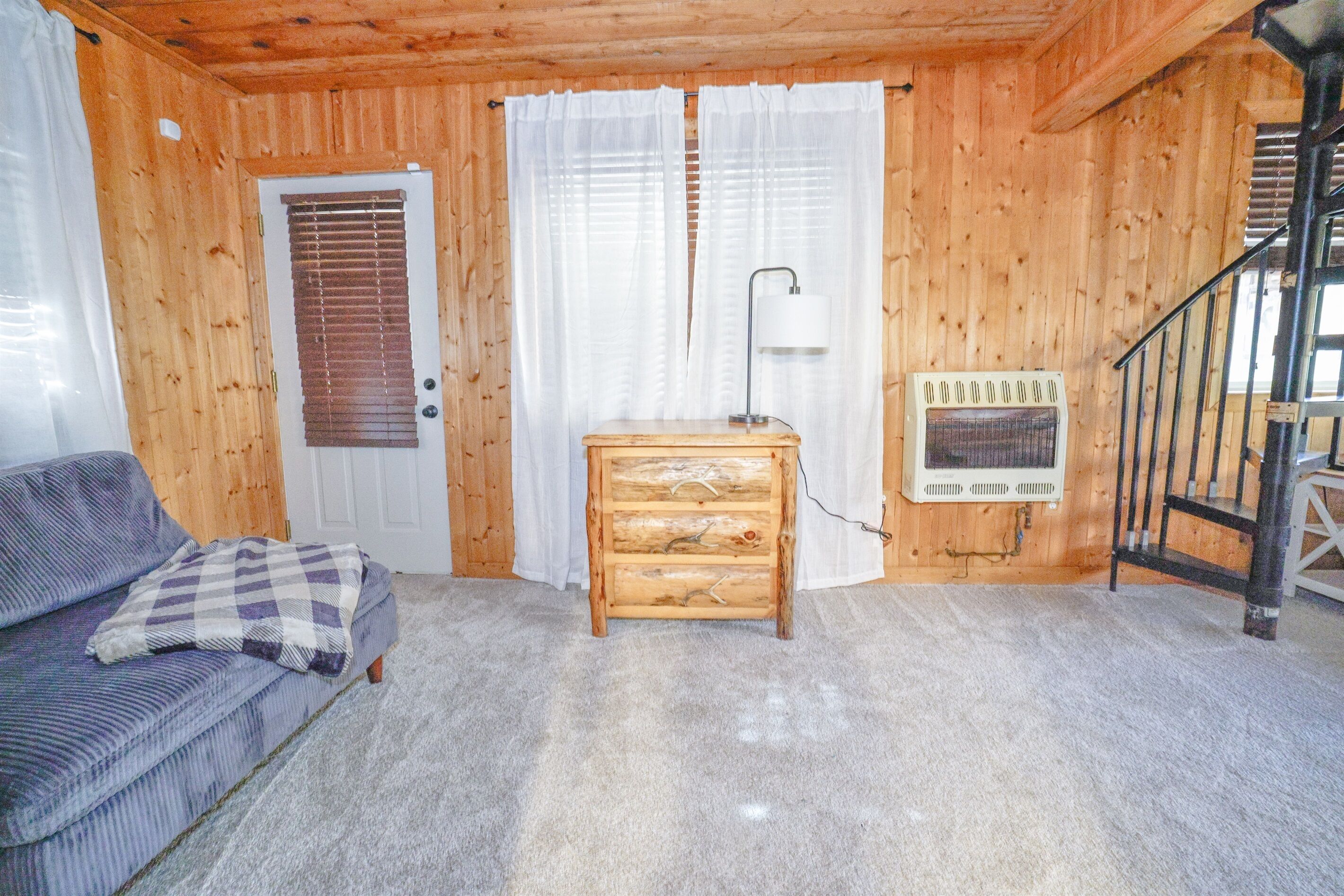 A log cabin interior with a wooden door, a white radiator, a lamp, and a checkered cushion on a sofa.