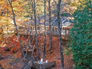 A treehouse structure with wooden platforms and a ladder, surrounded by autumn foliage.