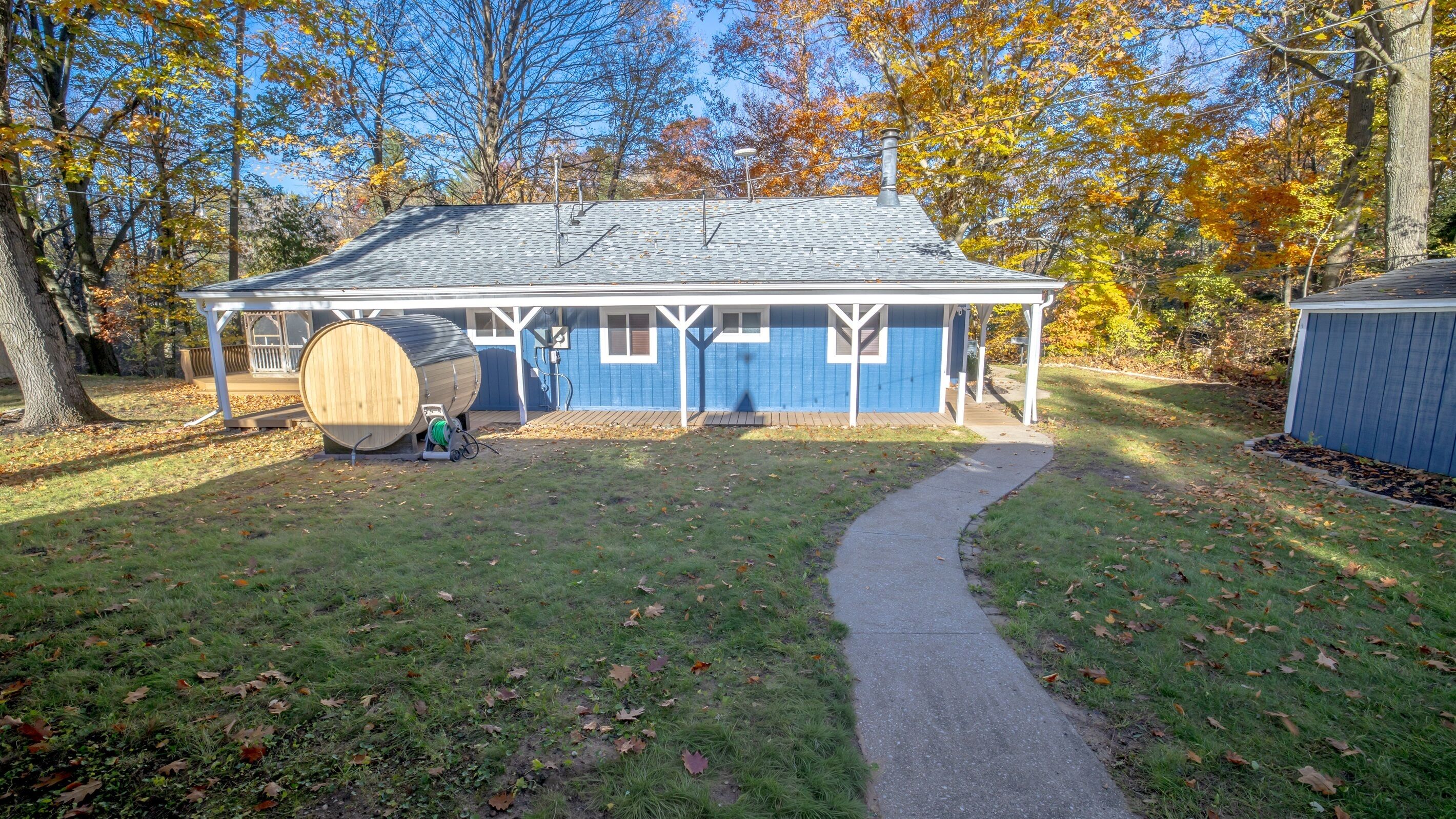 A house with a covered porch, a barrel, and a pathway leading to the house.