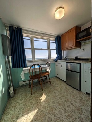 A kitchen with a window, a chair, a table, and a refrigerator. - Wake to Waves in Beachfront Cottages with Beach Access in North Truro, Massachusetts (North Truro)