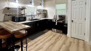 Une cuisine avec une table en bois, des tabourets de bar, un four à micro-ondes, une cuisinière et un évier.