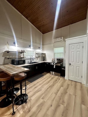 Une cuisine avec une table en bois, des tabourets de bar, un four à micro-ondes, une cuisinière et un évier.