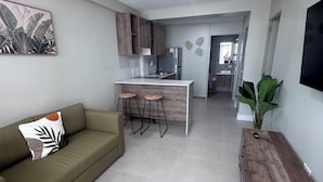 Ein modernes Wohnzimmer mit einer Couch, einem Holztisch und einer Küchenzeile im Hintergrund.
