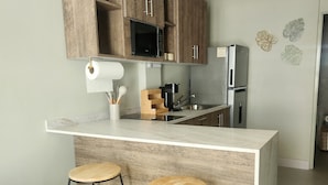 Eine moderne Küche mit Holzausstattung, einer eingebauten Mikrowelle, einer Kaffeemaschine und zwei Barhocker.