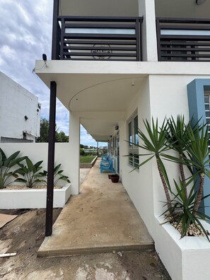 A building with a covered walkway, potted plants, and a blue chair. - Luna Del Mar Palmas - Near Crash Boat Beach (Borinquen)