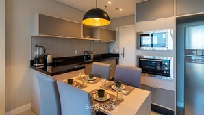 A modern kitchen with built-in appliances, a dining area with a table set for two, and a large pendant light. - House in Condo. w/ Garage in Rio Vermelho Tstedf0401 (Salvador)