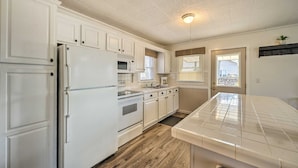 A kitchen with white cabinets, a refrigerator, a microwave, a stove, and a tiled countertop. - Round Lake | Fire Pit, Grill, Patio & Lake Access (Mecosta)