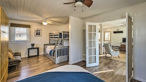 A bedroom with a bunk bed, a desk, a chair, a ceiling fan, and a door leading to another room. - Round Lake | Fire Pit, Grill, Patio & Lake Access (Mecosta)