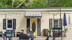 A building with a yellow door, black shutters, and outdoor seating with chairs and tables. - Round Lake | Fire Pit, Grill, Patio & Lake Access (Mecosta)