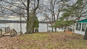A lakeside property with a dock, a covered deck, and a building with large windows. - Round Lake | Fire Pit, Grill, Patio & Lake Access (Mecosta)
