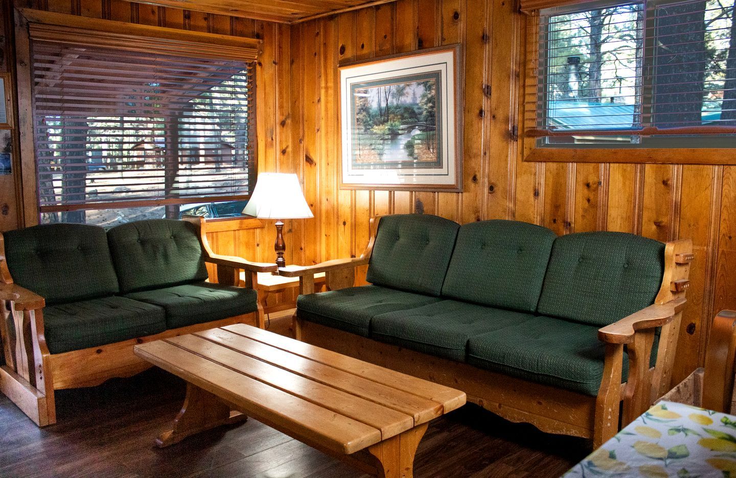 Interior de una cabaña de madera con un sofá, dos sillones, una mesa y una lámpara.