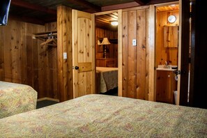 A wooden room with two beds, a wooden wardrobe, and a bathroom with a sink and mirror. - Cabin #2 (Flagstaff)