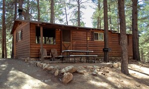 A rustic cabin with a picnic table and chairs, surrounded by a natural forest setting. - Cabin #2 (Flagstaff)