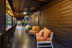 A wooden deck with a ceiling fan, outdoor seating with cushions, and a railing. - Banjo Bend Lodge | Pool, Spa, Sauna & Games (Broken Bow)