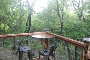 A wooden deck with a metal railing, two chairs, and a table. - Enchanting Pecan Treehouse with Creek Views near Forestburg, Texas (Forestburg)