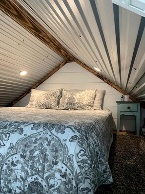 A bedroom with a bed, pillows, a nightstand, and a ceiling with wooden beams. - Enchanting Pecan Treehouse with Creek Views near Forestburg, Texas (Forestburg)