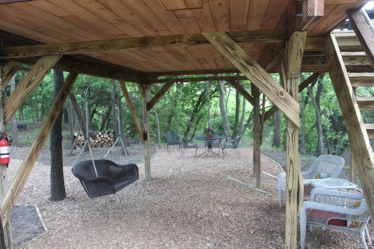 A wooden structure with a swing, outdoor seating, and a fire extinguisher.