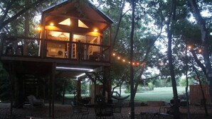 Une cabane en bois dotée d’un balcon, d’un espace salon extérieur et de guirlandes lumineuses.