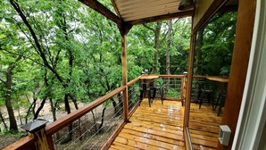 Une terrasse en bois avec une rambarde, une table et des chaises, entourée d’arbres.
