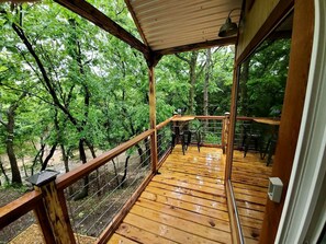 Eine Holzterrasse mit Geländer, einem Tisch und Stühlen, umgeben von Bäumen.