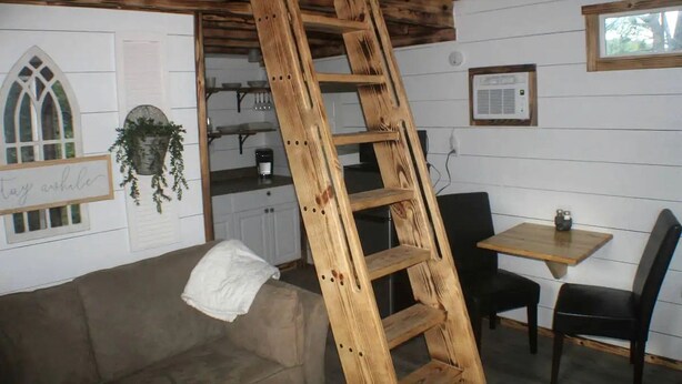 Un espace de vie de style « loft », doté d’une échelle en bois, d’un coin cuisine, d’un espace repas et d’une fenêtre offrant une vue agréable.