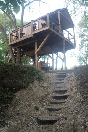 A wooden treehouse with a staircase leading up to it, surrounded by trees. - Enchanting Pecan Treehouse with Creek Views near Forestburg, Texas (Forestburg)