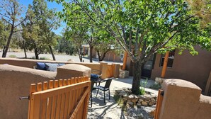 Un patio con una puerta de madera, un muro de piedra, un árbol y un área de patio con una mesa y sillas.