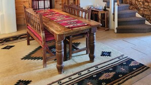 Un comedor con mesa y bancos de madera, una escalera y una pared de piedra.