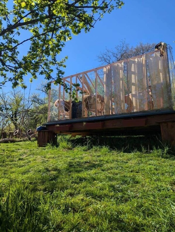A wooden platform with a metal railing, surrounded by grass and trees.