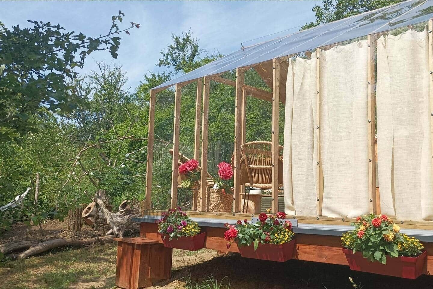 A greenhouse structure with a wooden frame, a glass enclosure, and a chair inside.
