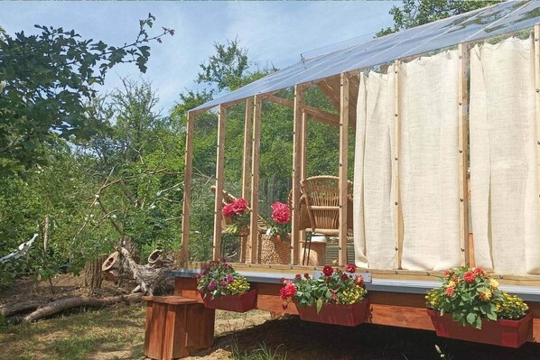 A greenhouse structure with a wooden frame, a glass enclosure, and a chair inside.