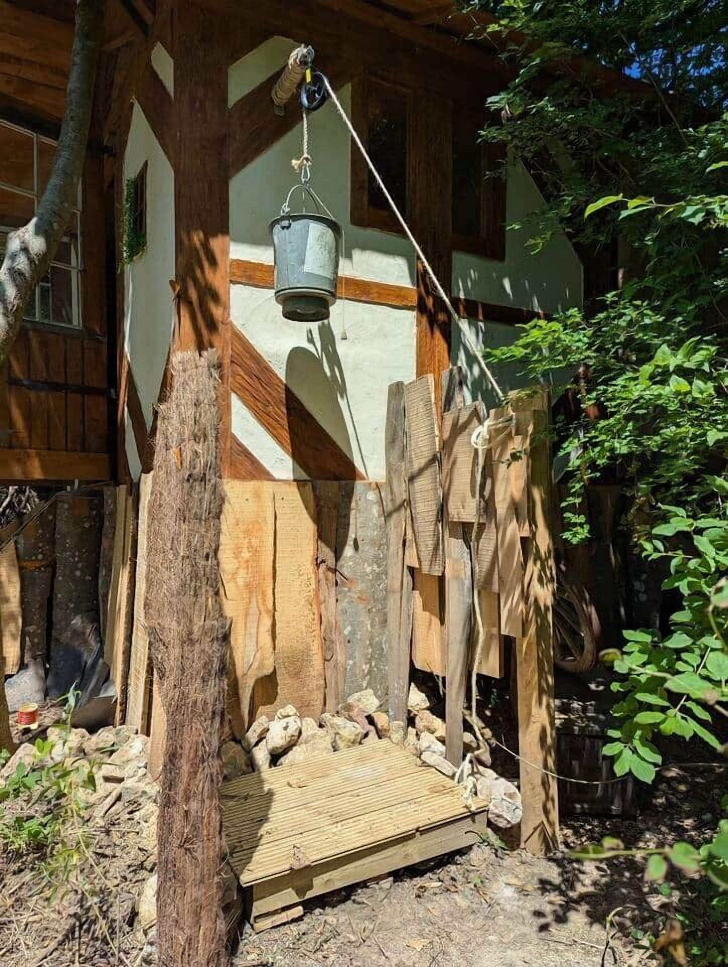 Eine rustikale Holzkonstruktion mit einem hängenden Eimer, einer hölzernen Bank und einem Baumstumpf.