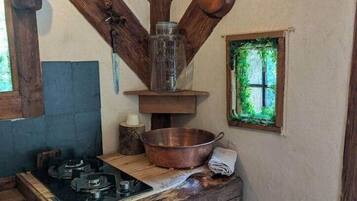 Een rustieke keuken met een houten fornuis, koperen pannen die aan het plafond hangen, en een raam met uitzicht op groen.